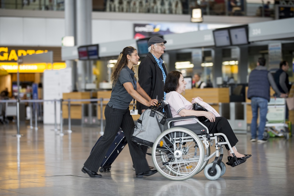 Passagierin mit eingeschränkter Mobilität im Rollstuhl wird von einer Mitarbeiterin im Terminal betreut