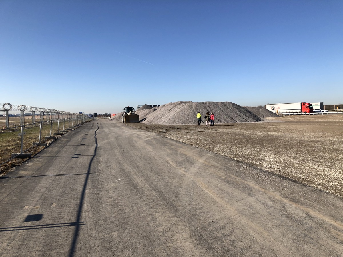 Blick auf die Baustelle mit Lagerplätzen neben der Autobahn und dem Flughafen