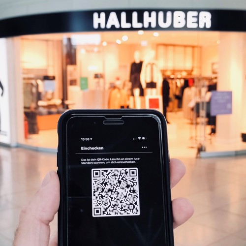 Hand hält Smartphone mit LucaApp vor einem Shop