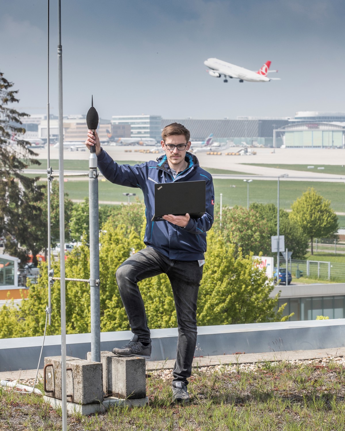 Ein Mitarbeiter des Flughafen Stuttgart steht neben einer Fluglärmmessanlage und überprüft die Daten auf seinem Laptop. 