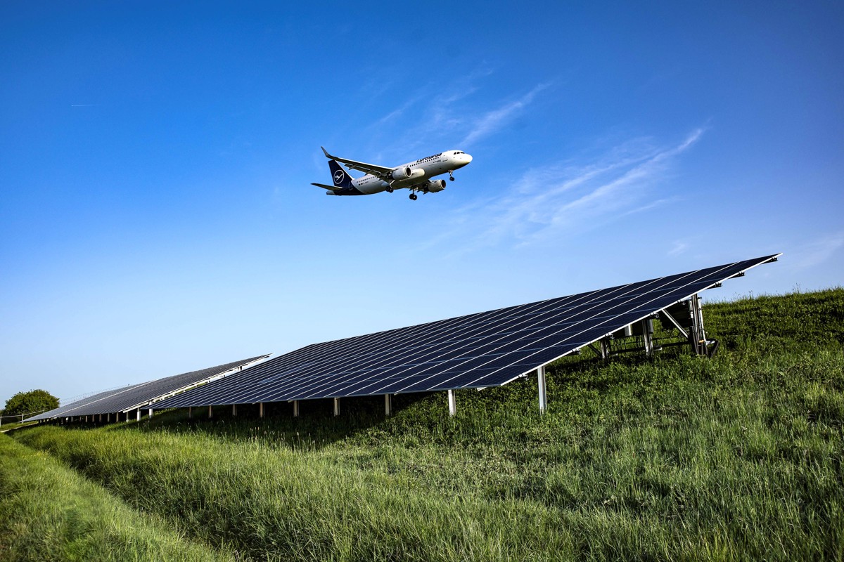 Ein Flugzeug fliegt über eine Solaranlage auf einer grünen Wiese.